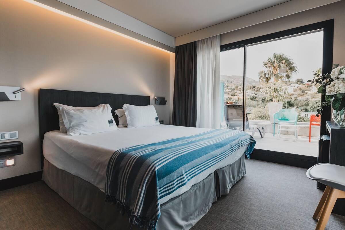 A modern hotel room with a large bed, a desk, and a view of the outdoors.