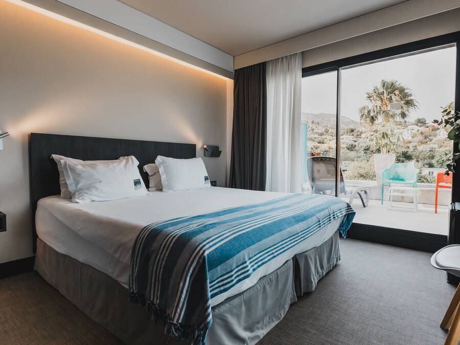 A modern hotel room with a large bed, a desk, and a view of the outdoors.