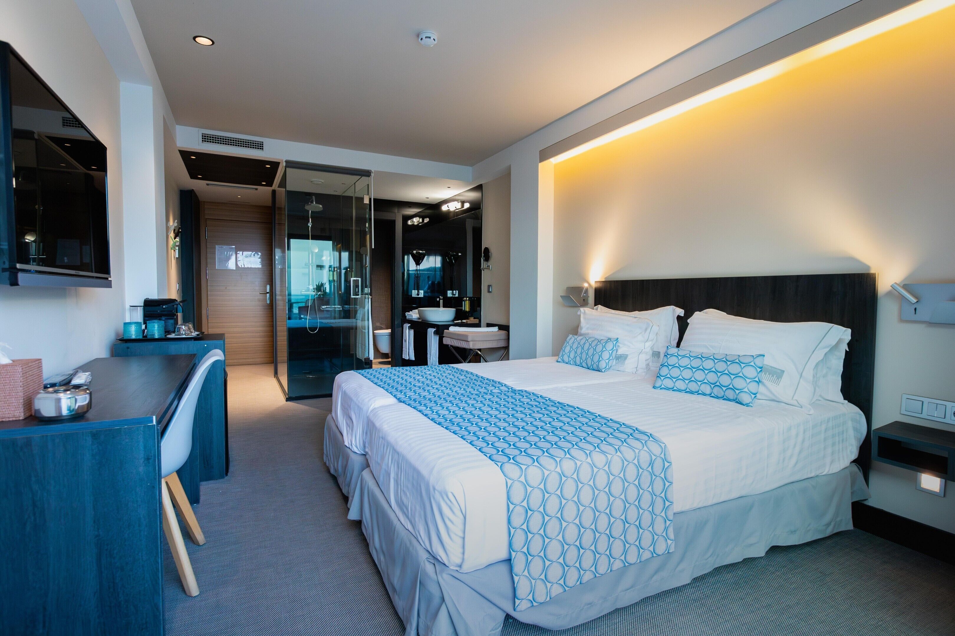 A modern hotel room with a large bed, a desk, a shower area, and a bathroom.