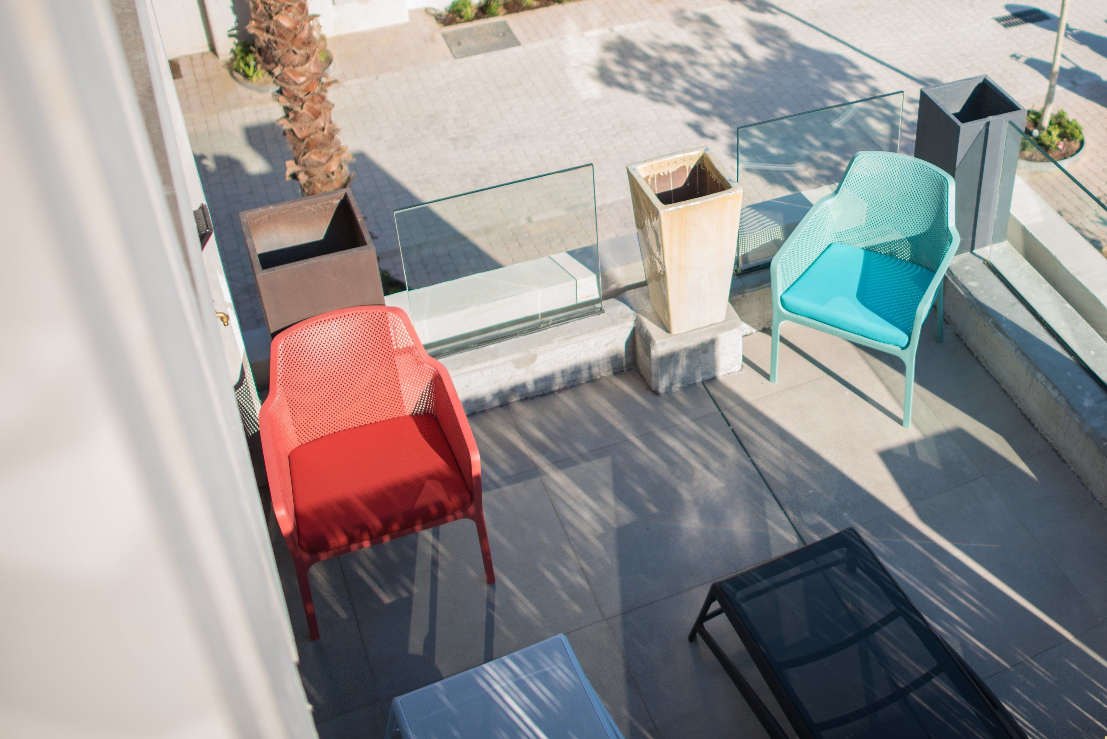Ein Balkon mit einem roten Stuhl, einem blauen Stuhl und einem Glastisch.