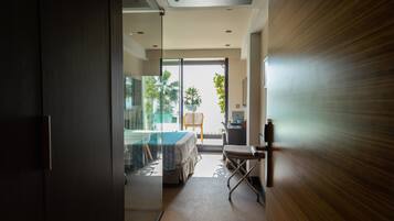 A modern hotel room with a glass door leading to a balcony, a bed, a desk, and a chair.