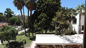 An outdoor patio area with tables and chairs, surrounded by palm trees and a building in the background.