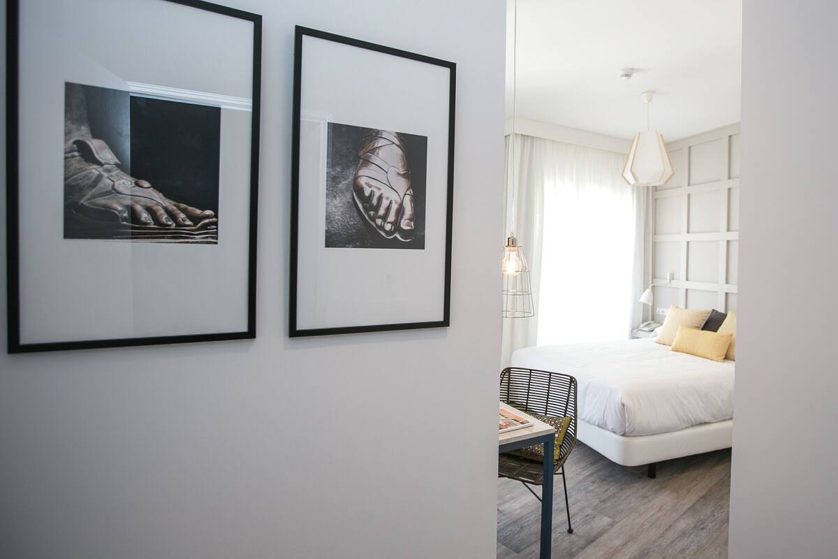 A modern bedroom with a white bed, a side table, and two framed artworks on the wall.