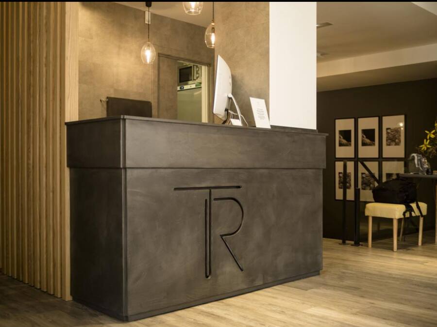 Una recepción con un gran logotipo en forma de 'R', un interior moderno con suelo de madera e iluminación colgante.