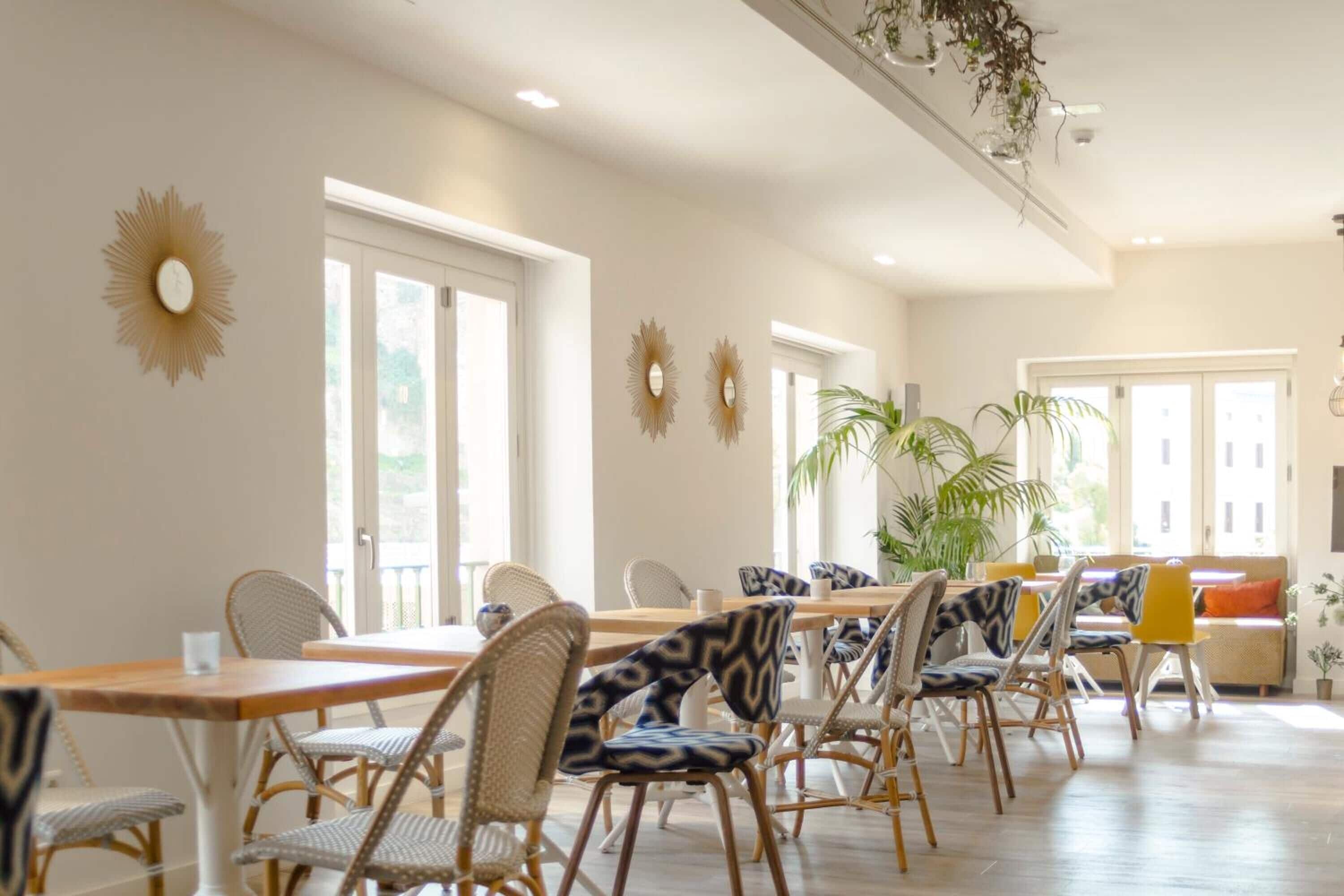 Un comedor amplio con una larga mesa de madera y sillas de mimbre, ventanas grandes y espejos decorativos en las paredes.