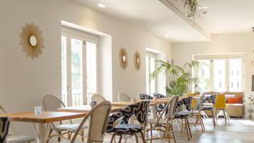 Un comedor amplio con una larga mesa de madera y sillas de mimbre, ventanas grandes y espejos decorativos en las paredes.