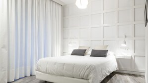A modern bedroom with a large bed, white curtains, and a wooden floor.