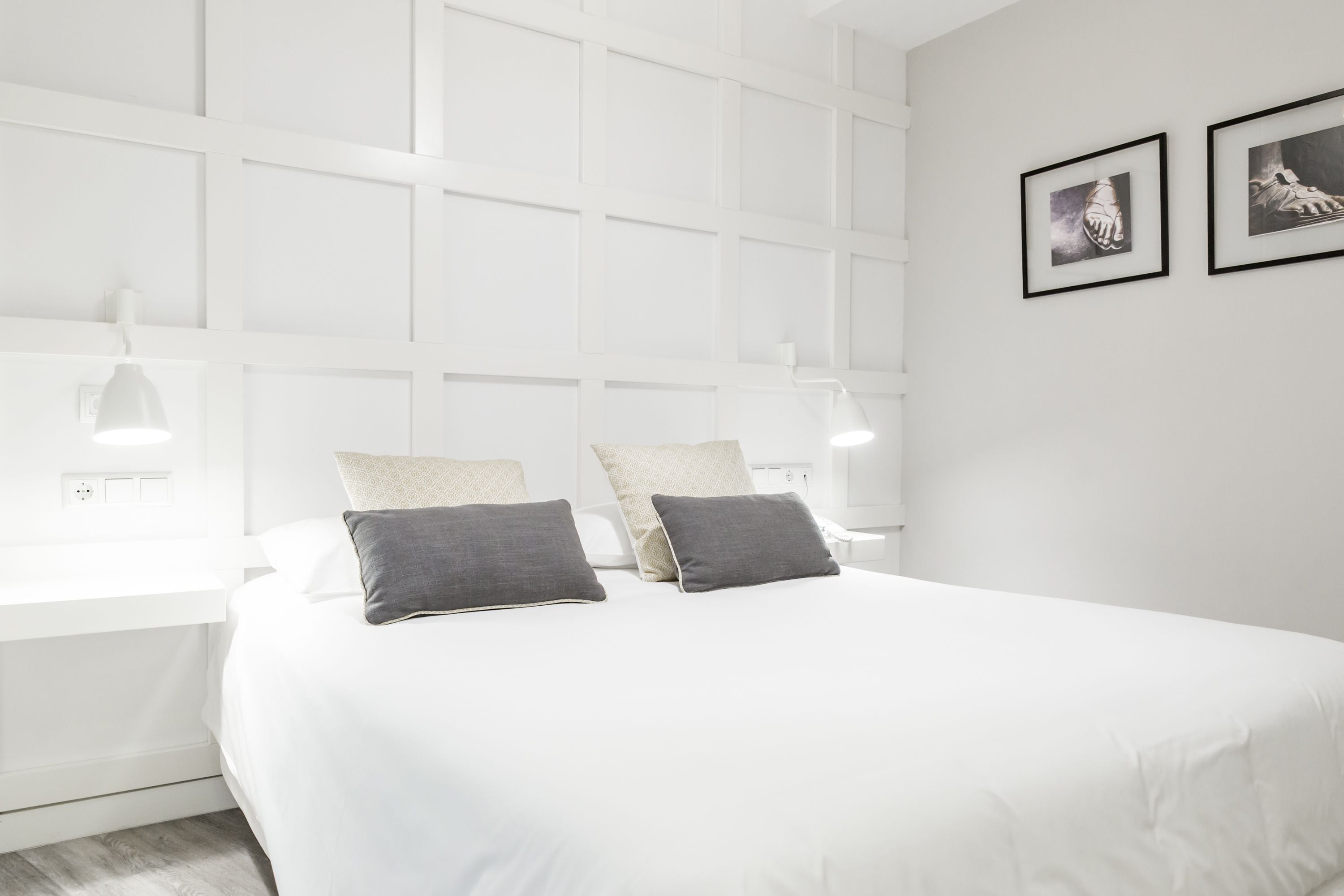 Un dormitorio moderno con una cama blanca, dos almohadas, una mesita de noche y lámparas de pared.