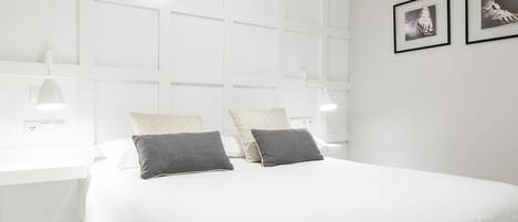 Un dormitorio moderno con una cama blanca, dos almohadas, una mesita de noche y lámparas de pared.