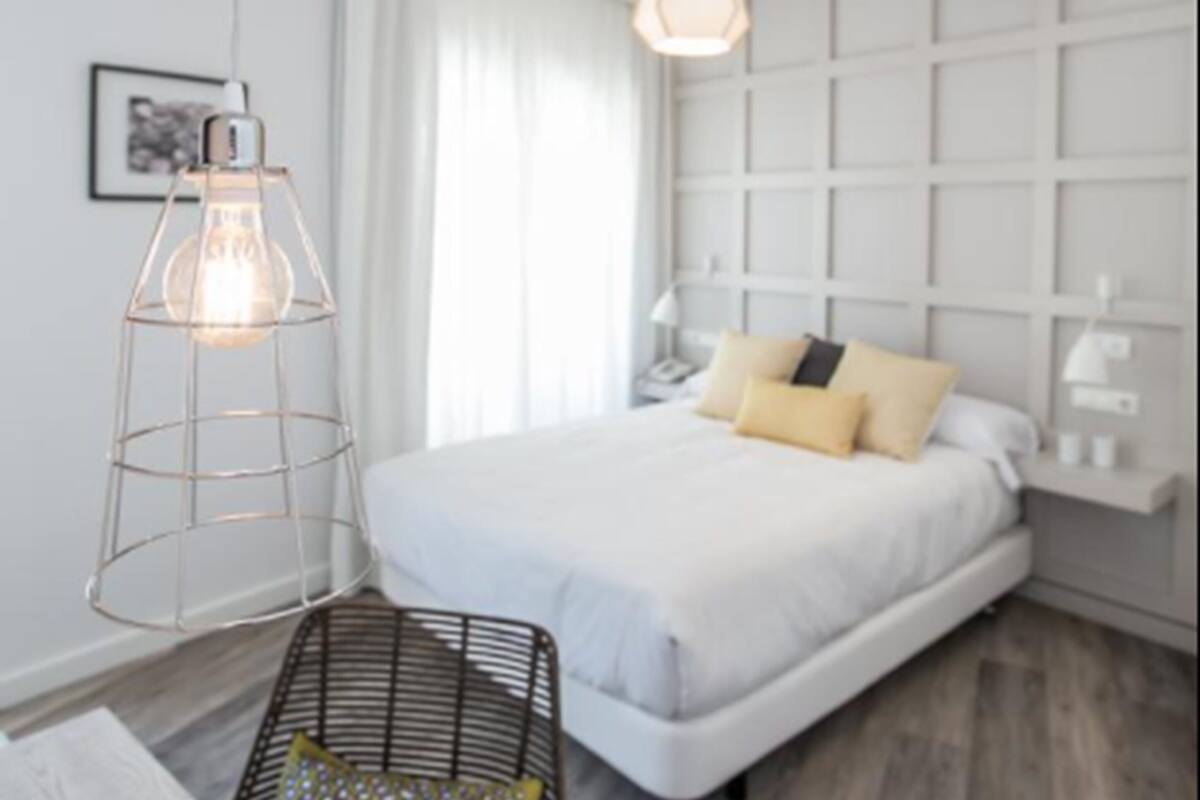 A modern bedroom with a bed, a hanging light fixture, and a bedside table.