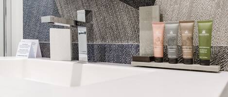 Un baño con un lavamanos moderno, un espejo y una variedad de artículos de aseo, incluyendo champú, acondicionador y gel de ducha.