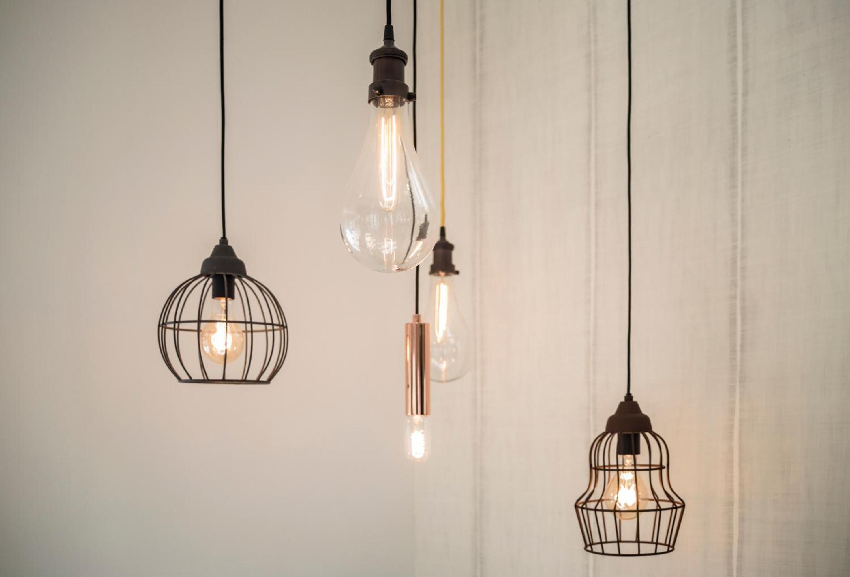 Trois luminaires suspendus, avec des ampoules apparentes, fixés sur un mur uni.