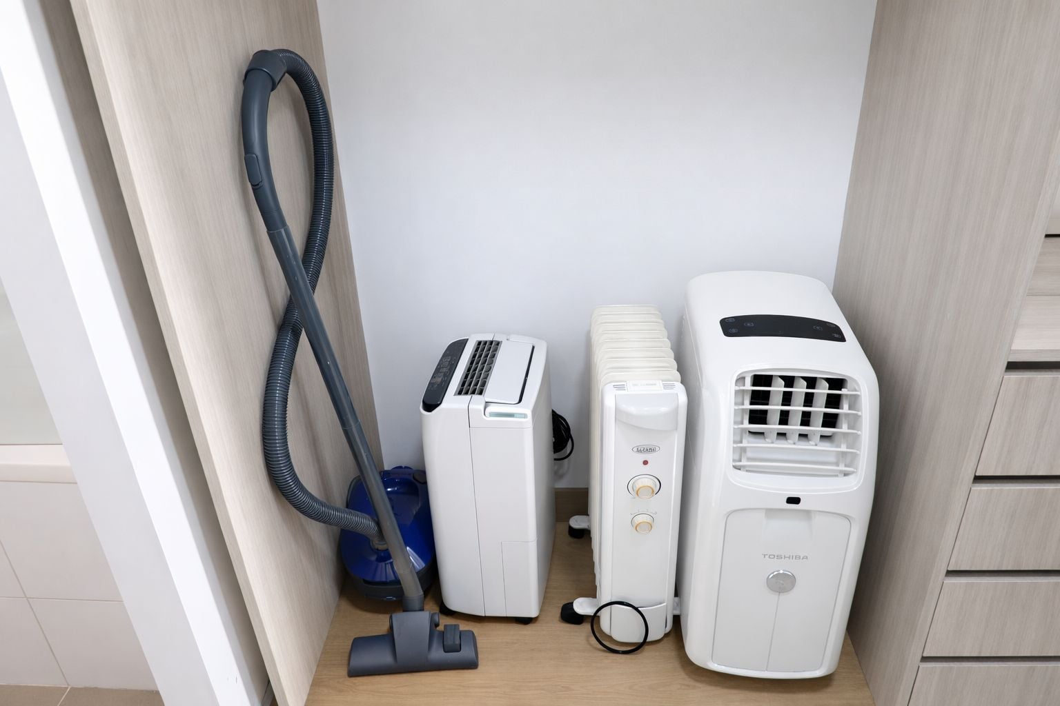 A compact room with a vacuum cleaner, a white heater, and a white air conditioner.