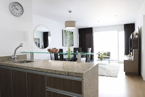 Una cocina moderna con encimeras de granito, un lavamanos integrado y una zona de comedor con una mesa y sillas de vidrio.