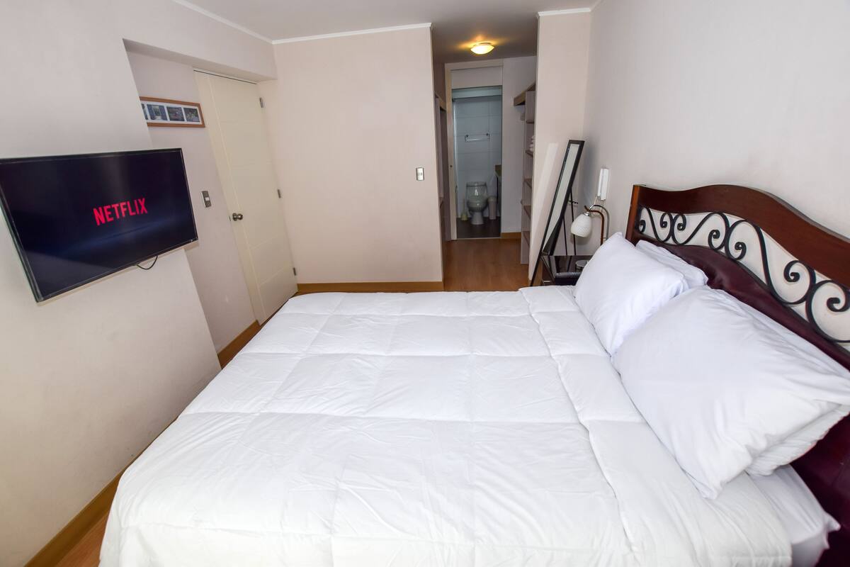 A bedroom with a bed, a TV mounted on the wall, and a door leading to a bathroom.