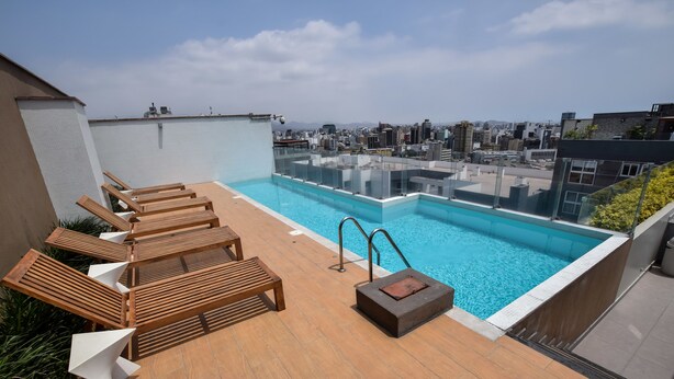 A rooftop pool with wooden loungers and a glass barrier. - Miraflores Nest Upper Pardo (Lima)