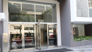 A modern building entrance with glass doors, a black mat, and a small garden area visible through the glass. - Miraflores Nest Upper Pardo (Lima)
