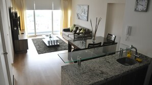 A modern living room with a glass dining table, a sofa with cushions, and a large window with curtains. - Miraflores Nest Upper Pardo (Lima)