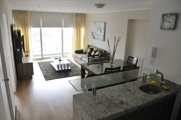 A modern living room with a glass dining table, a sofa with cushions, and a large window with curtains. - Miraflores Nest Upper Pardo (Lima)