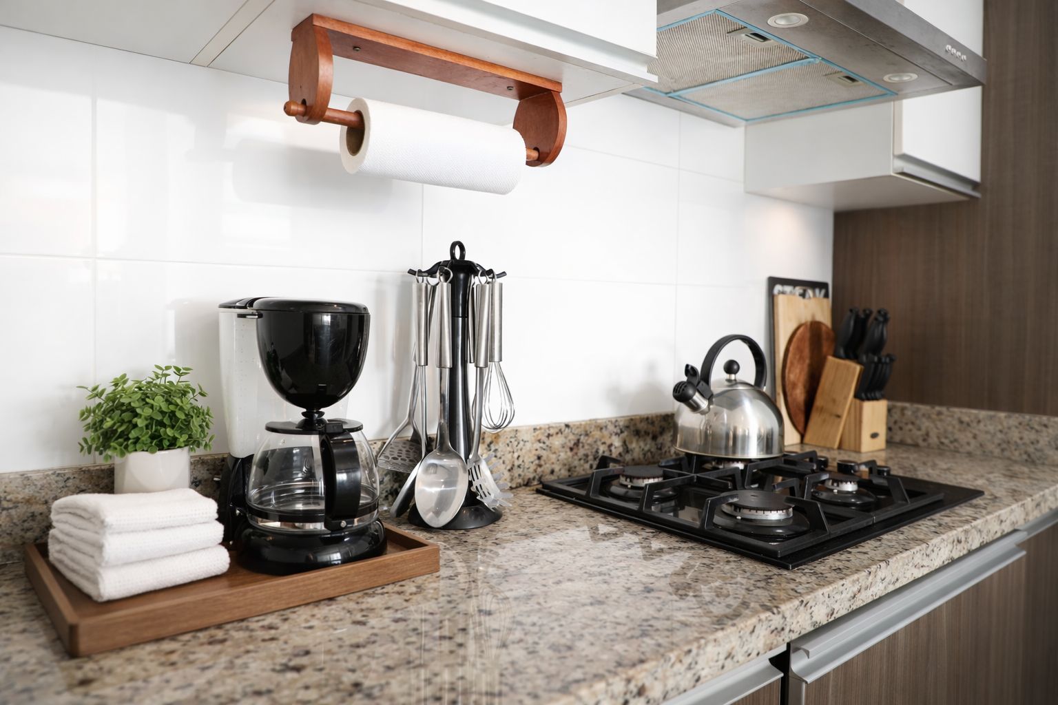 Una cocina con estufa a gas, cafetera, tetera y diversos utensilios.