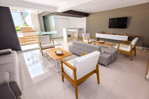 A modern living room with a sofa, chairs, a coffee table, a TV, and a kitchen area. - Miraflores NEST Upper Pardo, Rooftop Pool, Gym, AC, Near Kennedy Park (Lima)