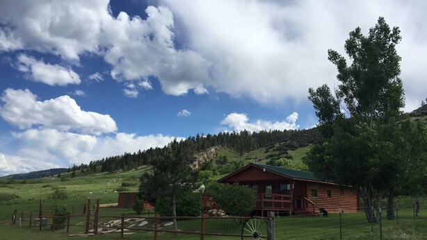 A wooden cabin with a green roof, surrounded by a fenced area with a bicycle wheel in the foreground. - Bighorn Lodge and Angler (Fort Smith)
