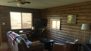 A cozy living room with a sofa, armchair, and a flat-screen TV. - Bighorn Lodge and Angler (Fort Smith)
