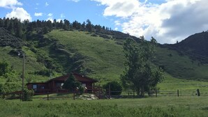 A rustic cabin with a wooden fence, surrounded by lush green fields and hills. - Bighorn Lodge and Angler (Fort Smith)