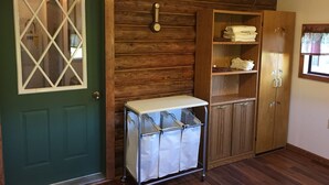 A room with a green door, wooden walls, a metal cart with white bags, wooden cabinets, and a clock on the wall. - Bighorn Lodge and Angler (Fort Smith)