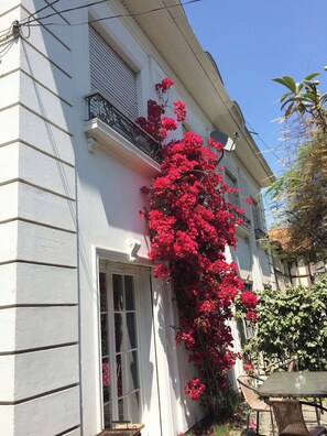 Un edificio con facciata bianca, un balcone adornato da fiori rossi e una finestra che si affaccia sul giardino.