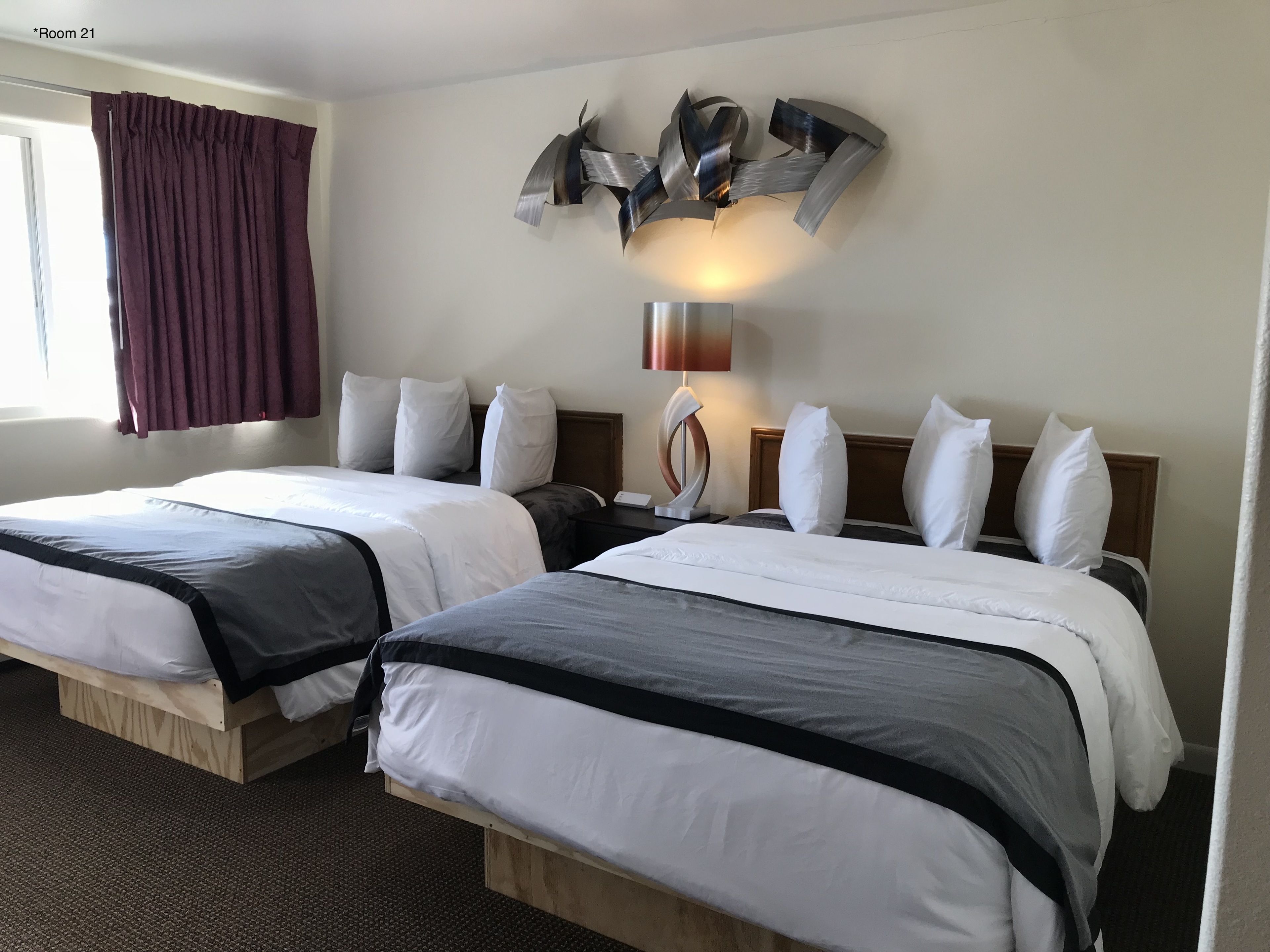 A hotel room with two beds, a modern wall art piece, a lamp, and a window with curtains.
