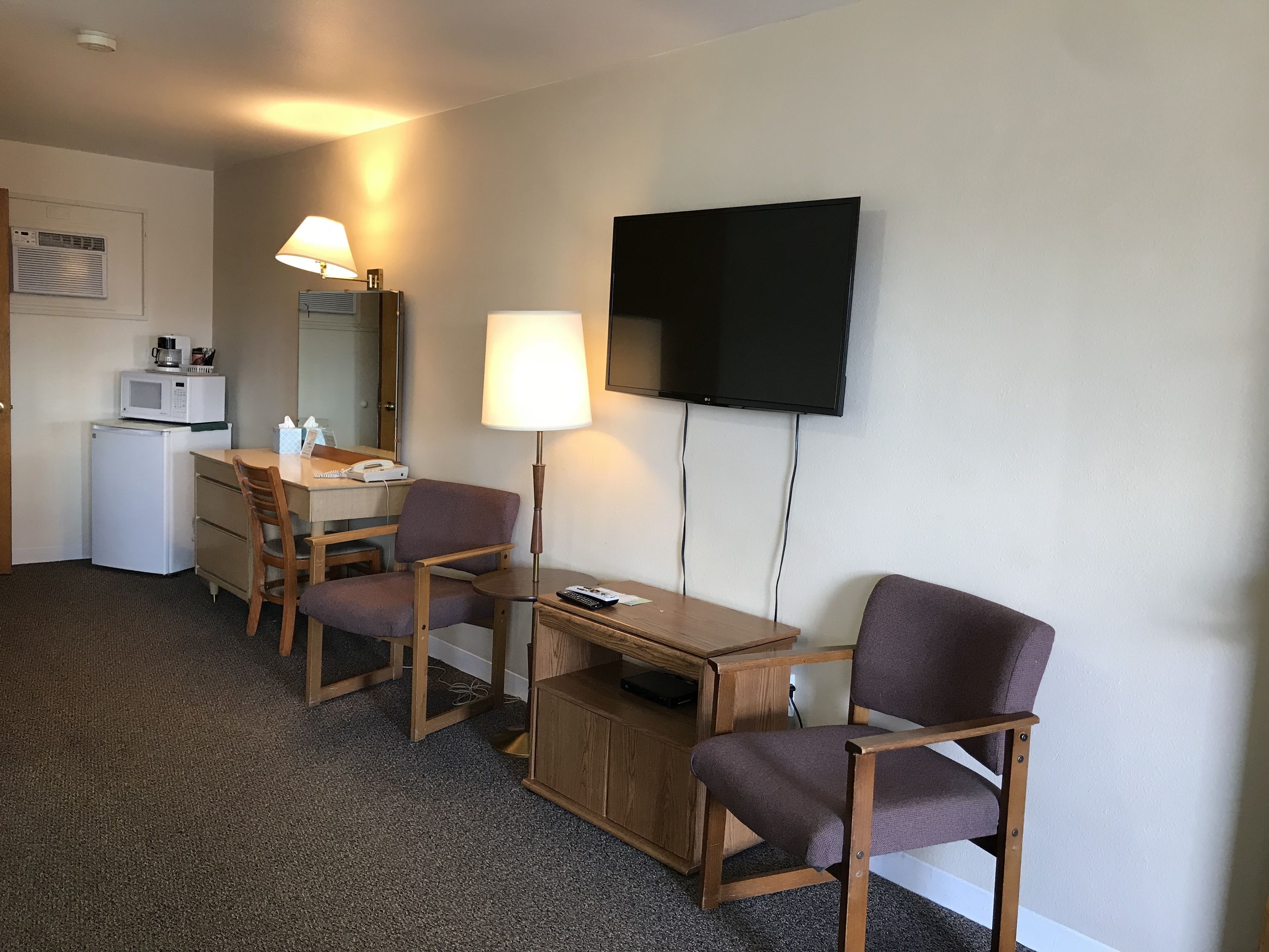 Een hotelkamer met een bureau, twee stoelen, een televisie, een lamp, een magnetron en een koelkast.