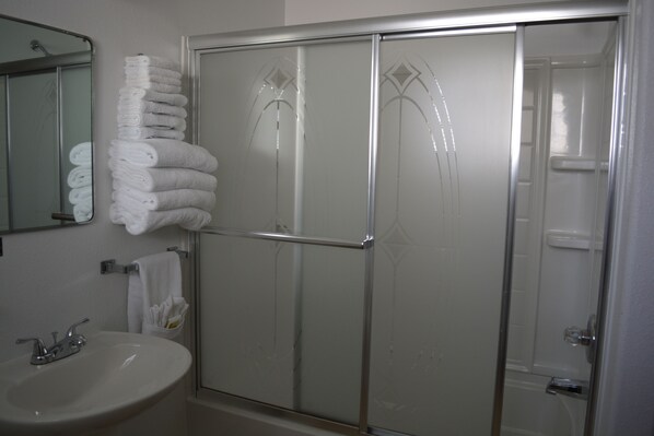 A bathroom with a glass shower enclosure, a sink, and a stack of folded towels. - Sage Motel (Newcastle)