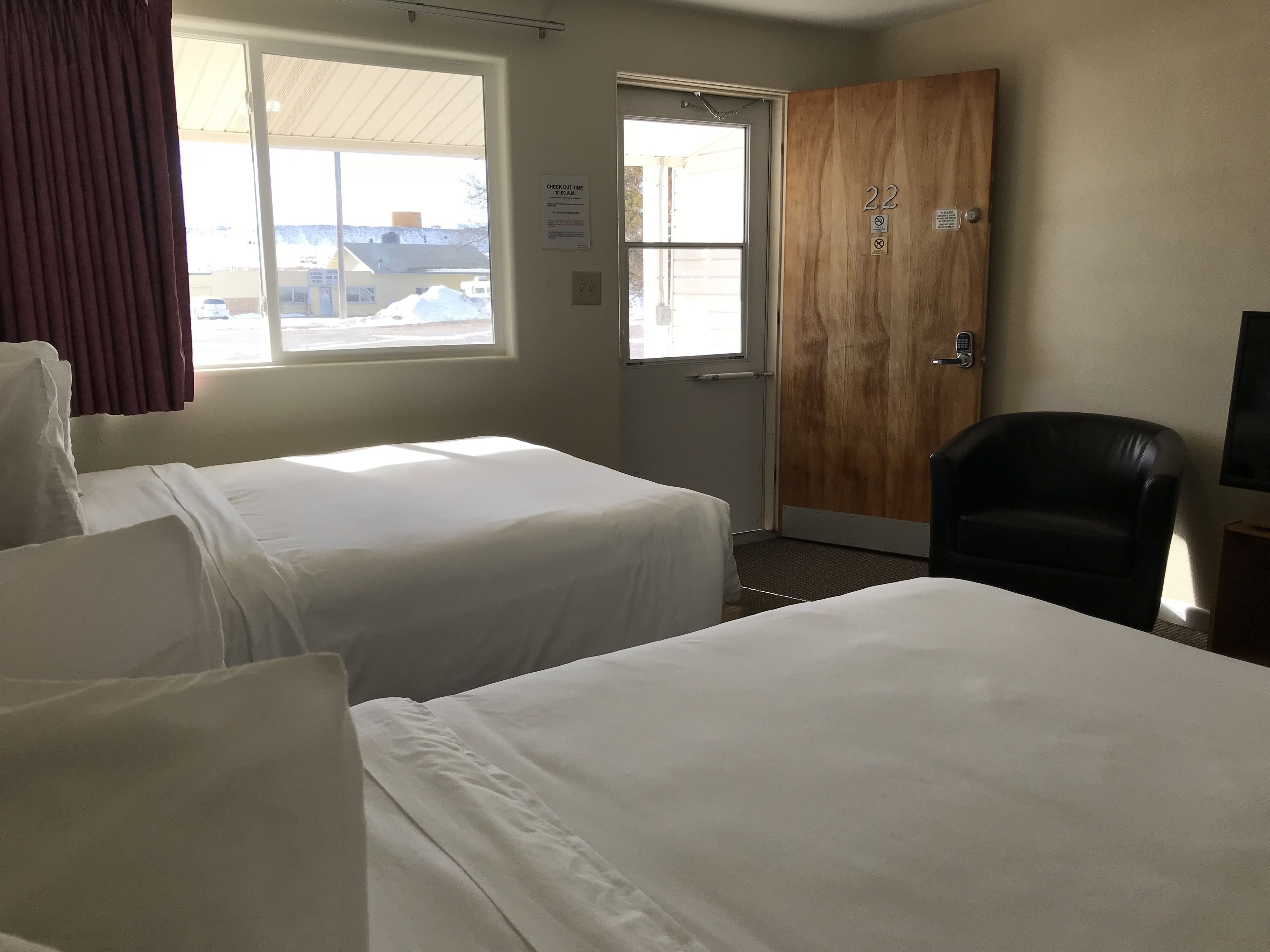 A hotel room with two beds, a wooden door, a chair, and a television.