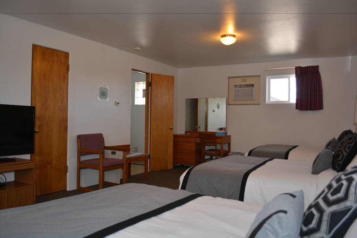 A hotel room with two beds, a desk, a chair, a television, a mirror, and a window with curtains.