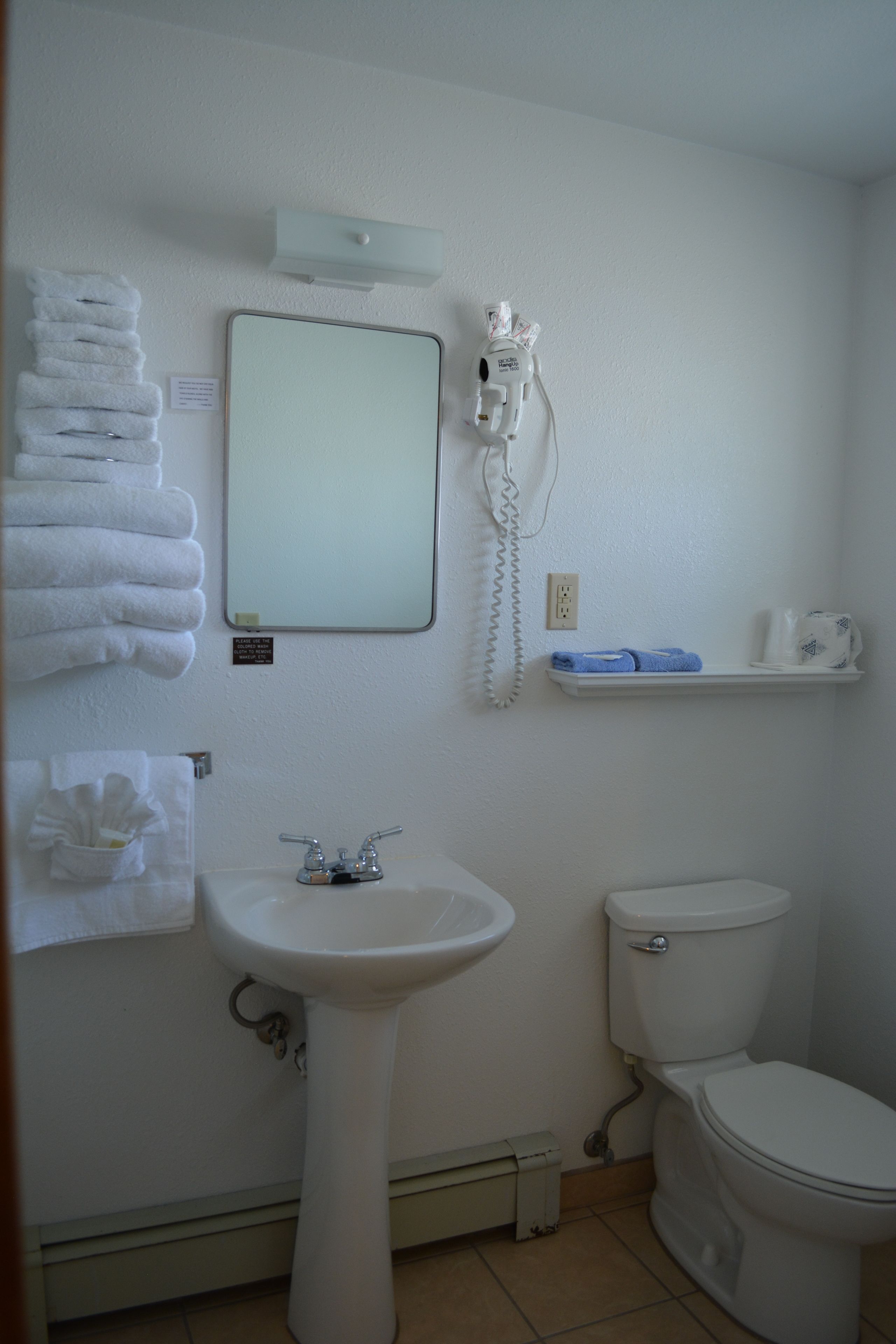 A bathroom with a sink, toilet, and a mirror. There are towels and a phone on the wall.