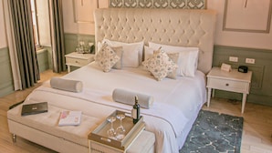 A neatly arranged bedroom with a tufted headboard, a bedside table with a lamp, a nightstand, a bedside table with a lamp, a tray with wine glasses and a bottle, and a book on the bed. - Illa Experience Hotel (Quito)