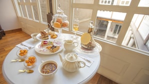 A table set with various pastries, a teapot, and a pitcher, positioned near a window with a view of buildings. - Illa Experience Hotel (Quito)