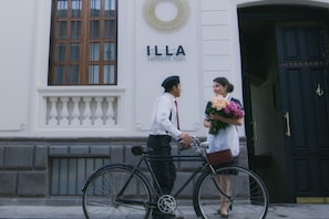 Un homme et une femme se tiennent devant un bâtiment sur lequel on peut lire l’inscription « ILLA EXPERIENCE HOTEL ».