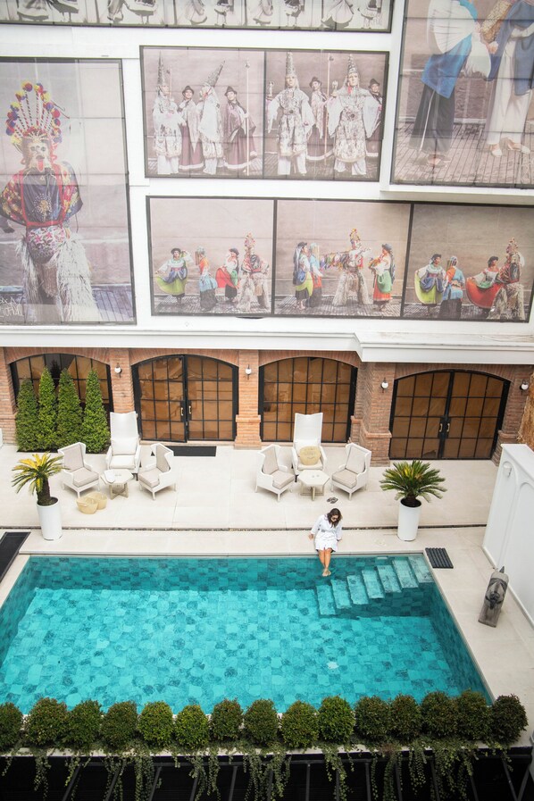 Une piscine sur le toit, avec des chaises longues, une personne qui passe, et des affiches d’opéra chinois traditionnel accrochées au mur.