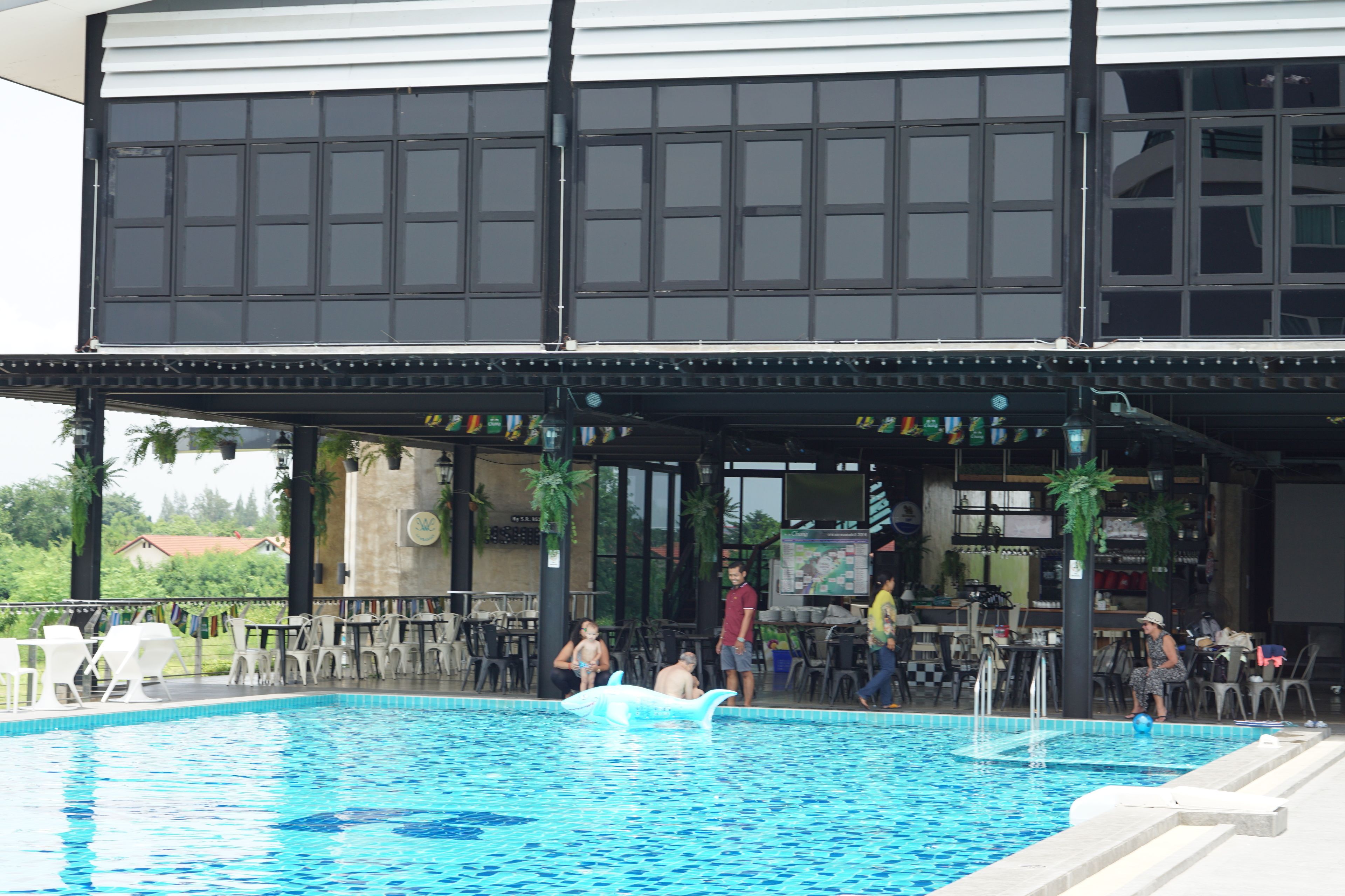 A swimming pool with lounge chairs and tables, a covered seating area, and a view of the surrounding landscape.