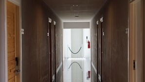 A hallway with wooden doors on both sides, a white tiled floor, and a glass railing in the center. - SR Residence Hotel (Phetchabun)