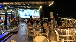 An outdoor dining area with tables and chairs, a pool, and a bar area with a TV screen. - SR Residence Hotel (Phetchabun)