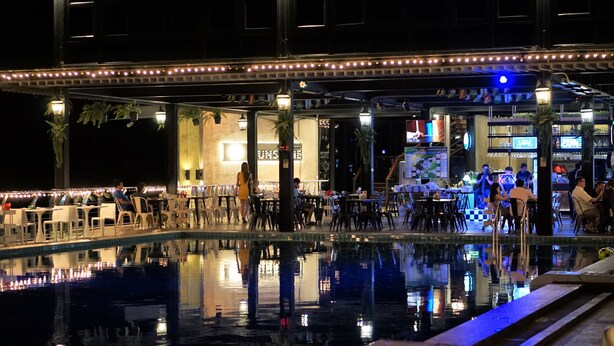 A nighttime poolside area with tables and chairs, a bar, and a stage for performances. - SR Residence Hotel (Phetchabun)