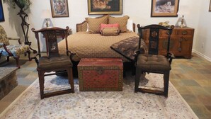 Une chambre avec un grand lit, deux chaises, une commode en bois et une table de chevet. Trois tableaux encadrés sont accrochés au mur.
