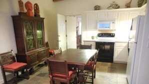 Un coin repas avec une table et des chaises en bois, un meuble avec des portes en verre et une cuisine avec des meubles et des appareils électroménagers blancs.