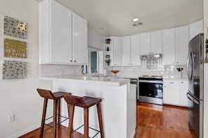 A modern kitchen with white cabinets, a stainless steel refrigerator, and a wooden island with stools. - Recently Renovated, Secluded Spot for a romantic rendezvous! Hot Tub, Fire pit (Wimberley)