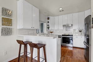 A modern kitchen with white cabinets, a stainless steel refrigerator, and a wooden island with stools. - Recently Renovated, Secluded Spot for a romantic rendezvous! Hot Tub, Fire pit (Wimberley)