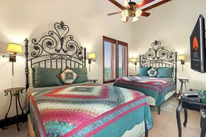 Una habitación con dos camas, cada una con una colcha estampada, un ventilador de techo y lámparas fijadas a la pared.