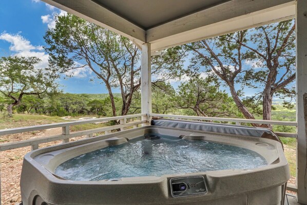 A hot tub under a covered area with a view of trees and a clear sky.